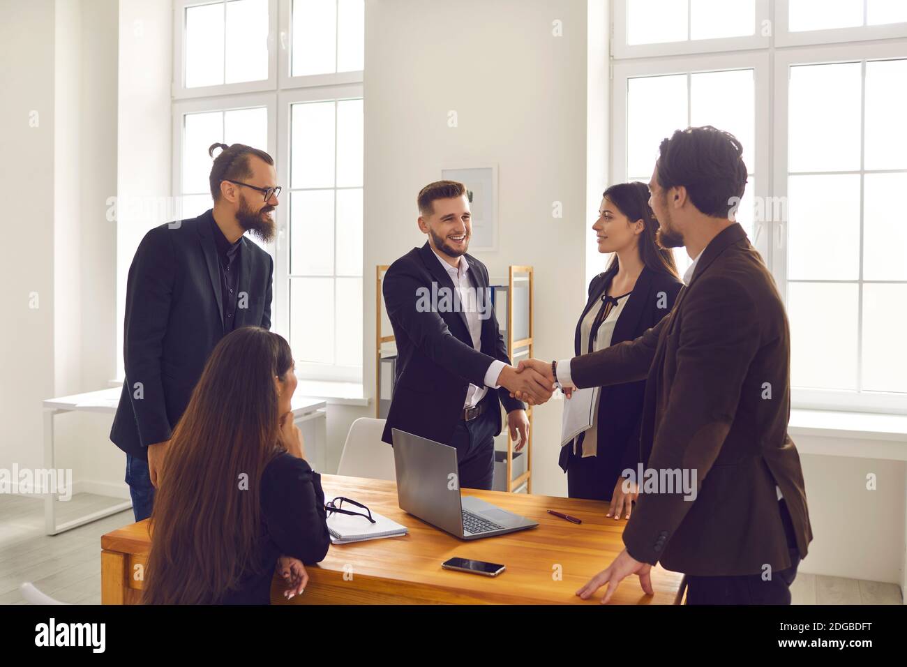 Young business people closing deal and shaking hands after successful negotiation in company office Stock Photo