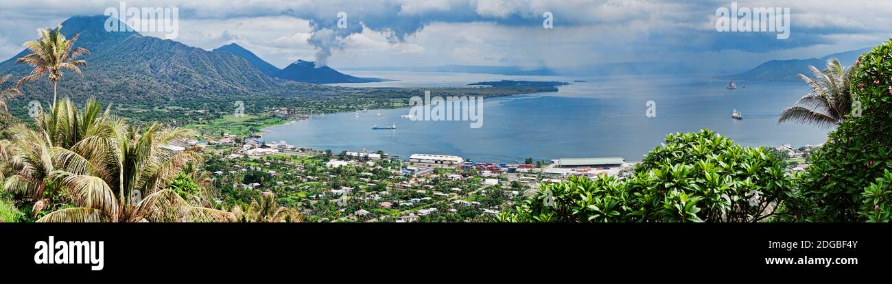 High angle view of a town on the coast with volcano in the background, Tavurvur, Rabaul, East New Britain, Papua New Guinea Stock Photo