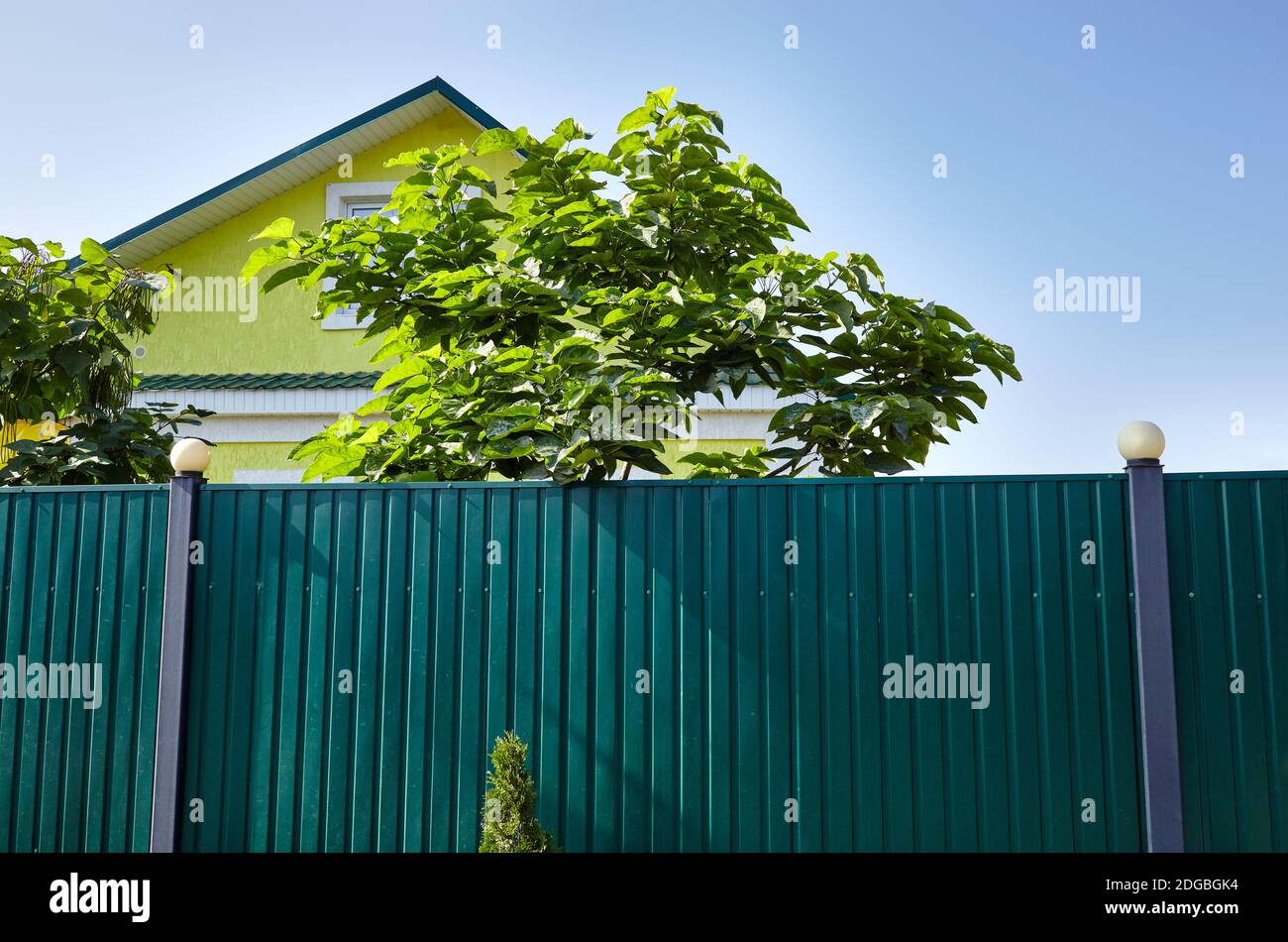 Facade of a yellow suburban building. Metal fence with lanterns against a blue sky Stock Photo