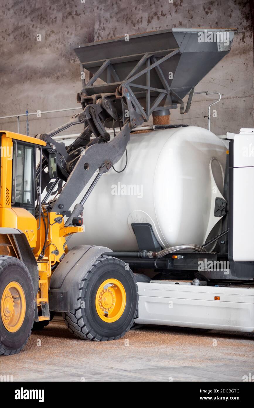 Tractor loading grain into truck at at grain processing plant warehouse