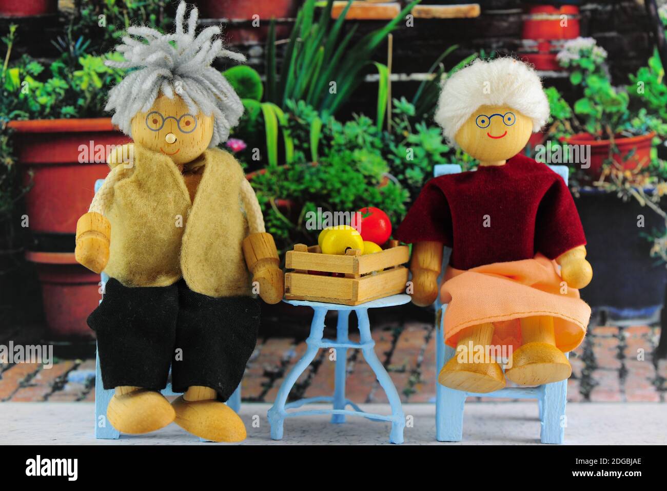 Older Couple sitting in Garden.  Garden Furniture and Wooden figurines / dolls. Stock Photo