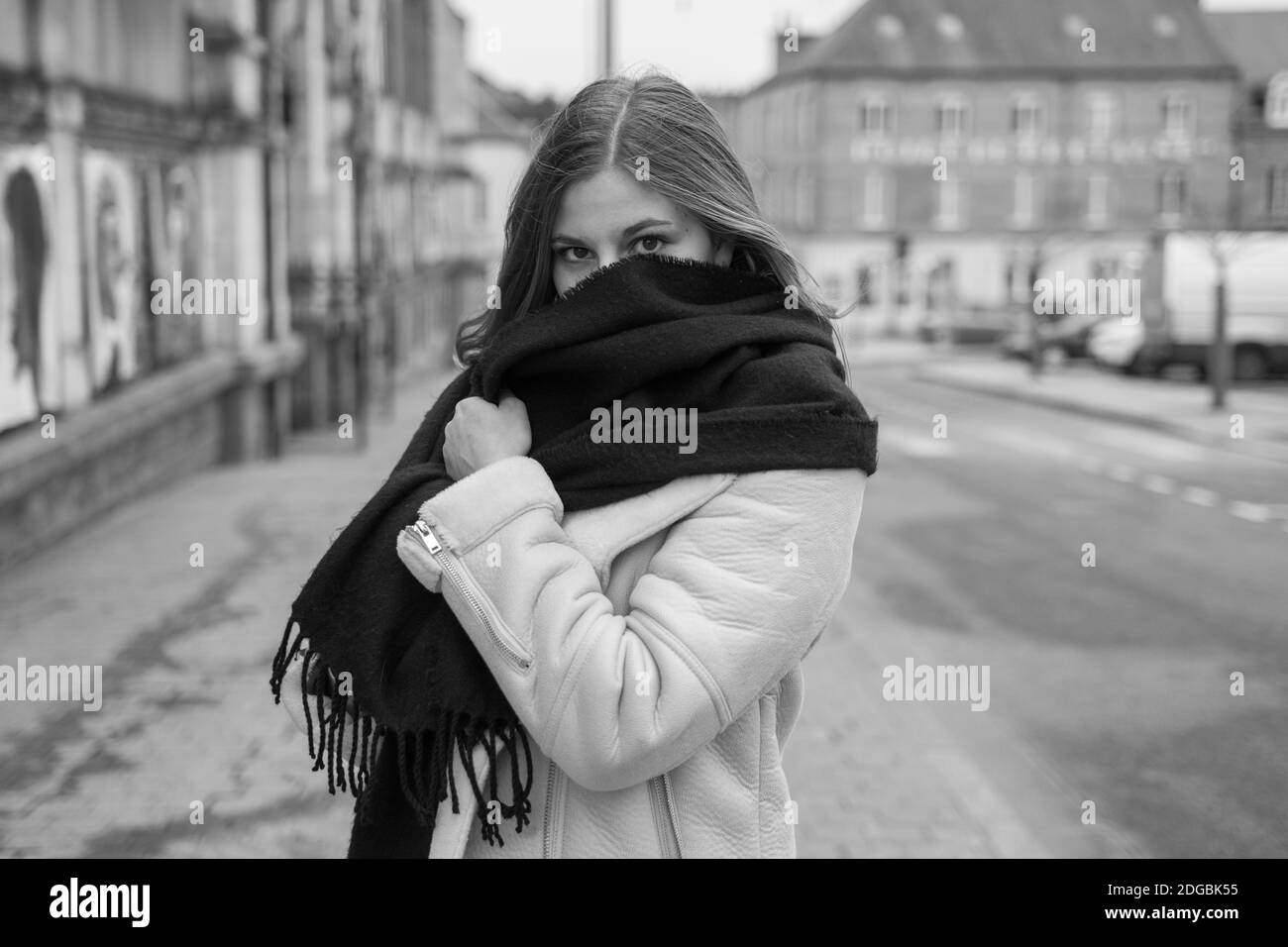 Beautiful young adult woman wearing a black scarf that is hiding the bottom of her face. She is looking at the camera. Black and White photography. Stock Photo