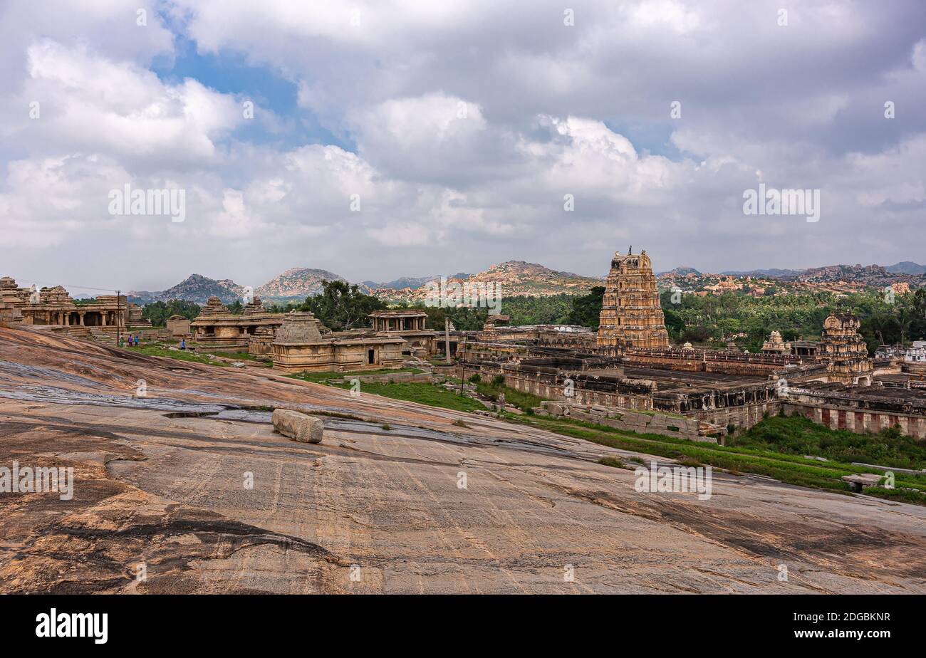 Hampi, Karnataka, India - November 4, 2013: Virupaksha Temple complex. Slanted rock plateau leading to landscape with said temple under blue cloudscap Stock Photo