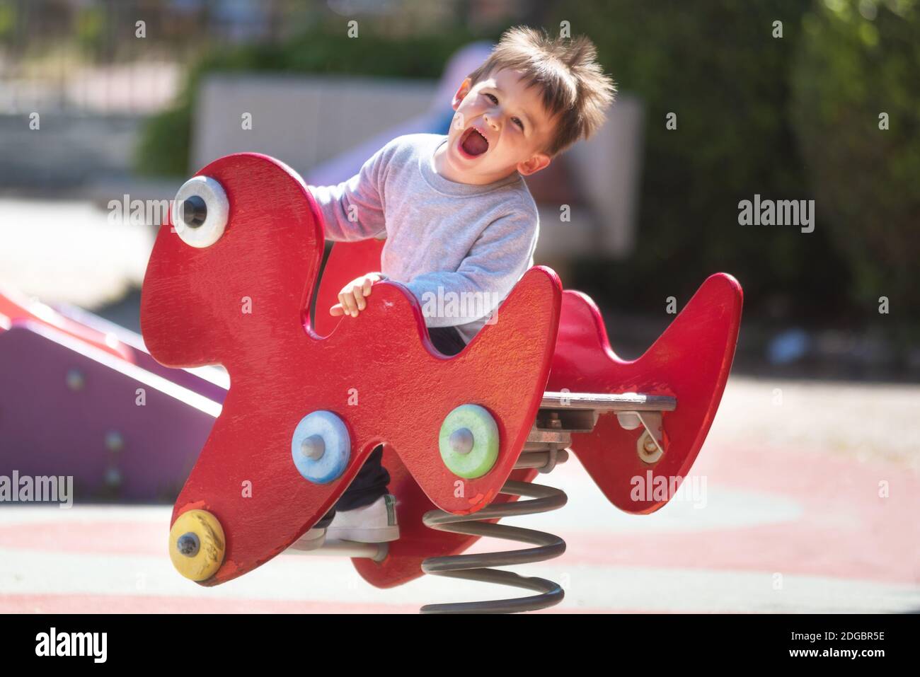 Cute happy baby boy with blond hair riding red spring rider or rocker ...