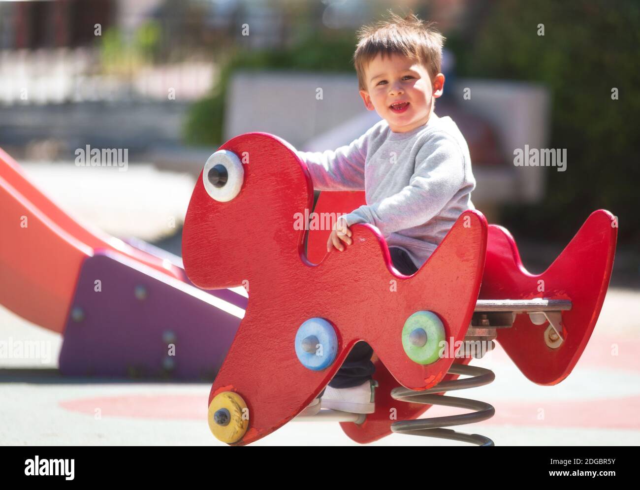 Baby Rider Outside Cute happy baby boy with blond hair riding red spring rider or rocker ...