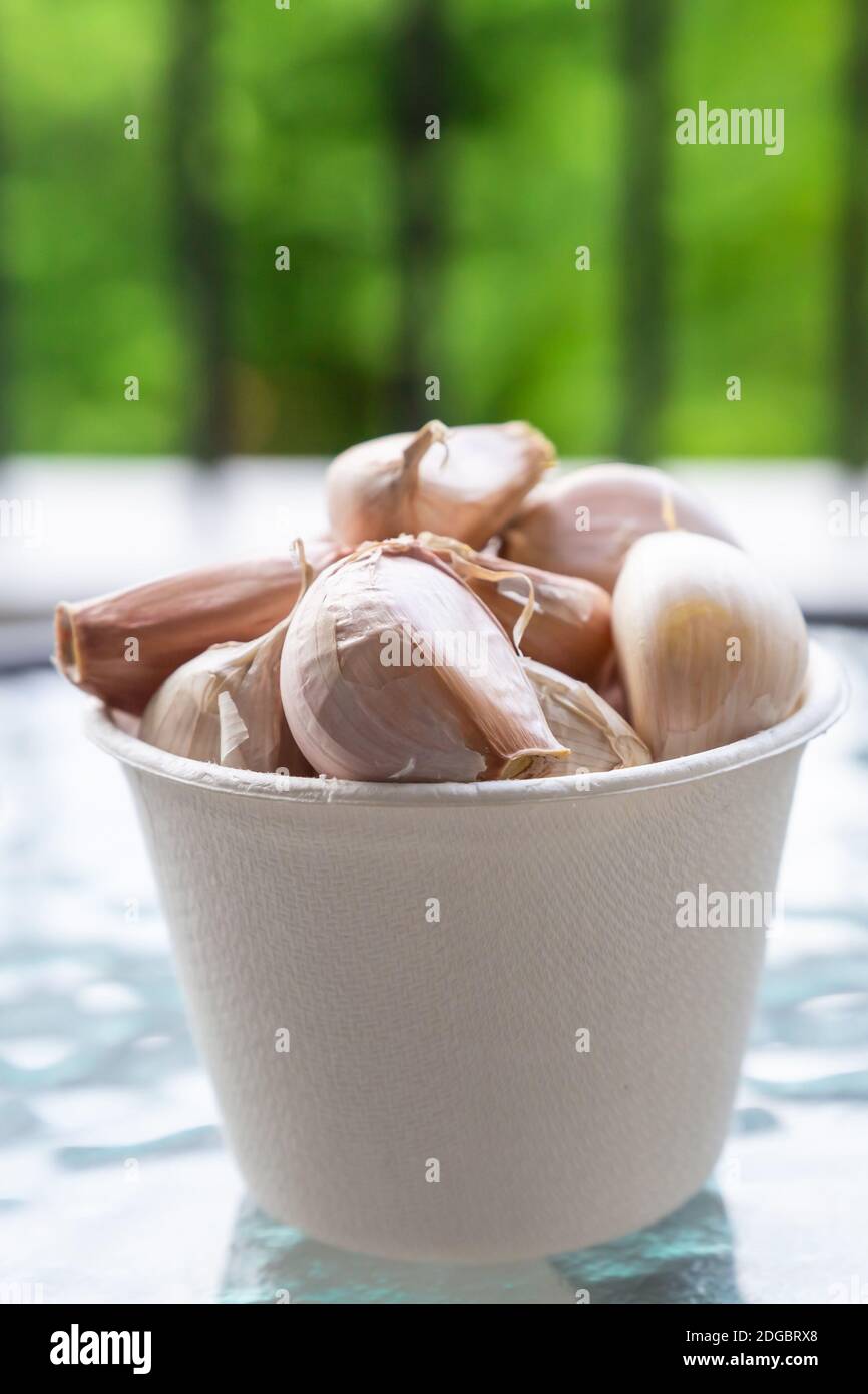 Garlic divided into slices piled into a paper bowl standing on a glass