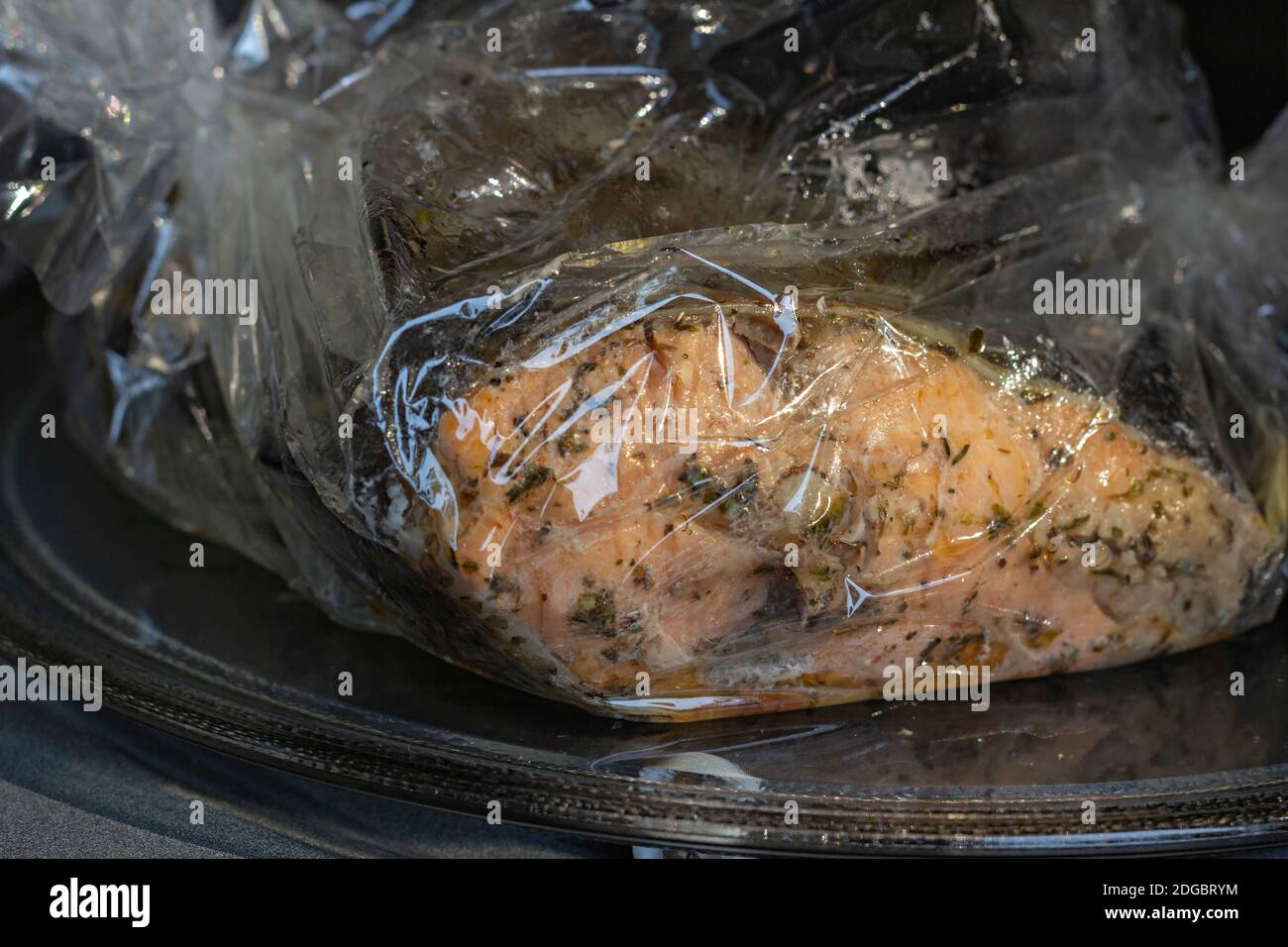 Spiced fresh trout fish wrapped in a baking sleeve in a microvawe oven, cooked, closeup view Stock Photo