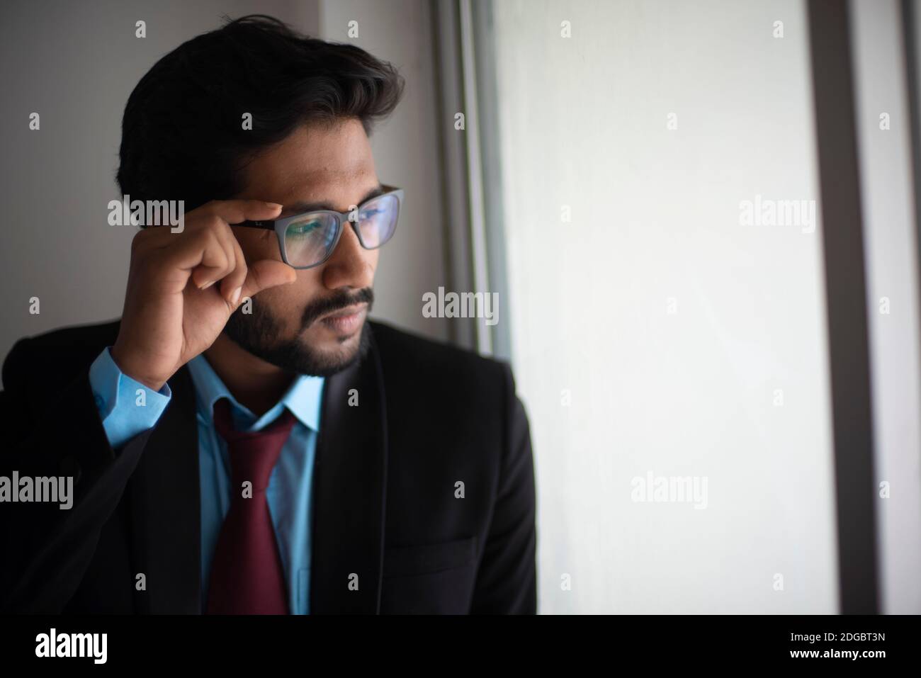 Portrait of an Indian Bengali tall, dark, handsome brunette young man in office wear is standing in front of a glass window in a corporate office/bpo Stock Photo