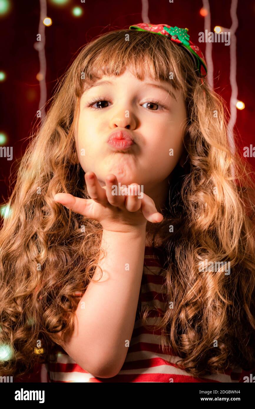 Portrait of a smiling girl blowing kisses in front of Christmas lights Stock Photo