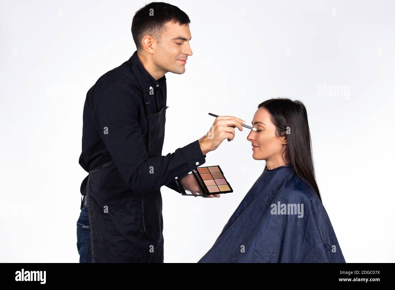A man being a makeup artist holds a cosmetic palette, works to a female