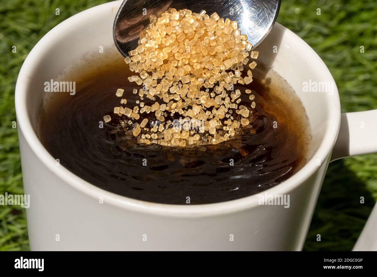 A teaspoon is pouring brown sugar into a cup of hot beverage, close up view. Sweetening the