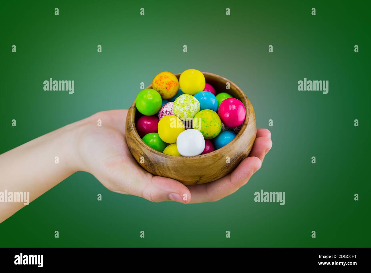 Bright candy chewing gum in a wooden bowl dish lies on the palm of hand on a green background macro Stock Photo