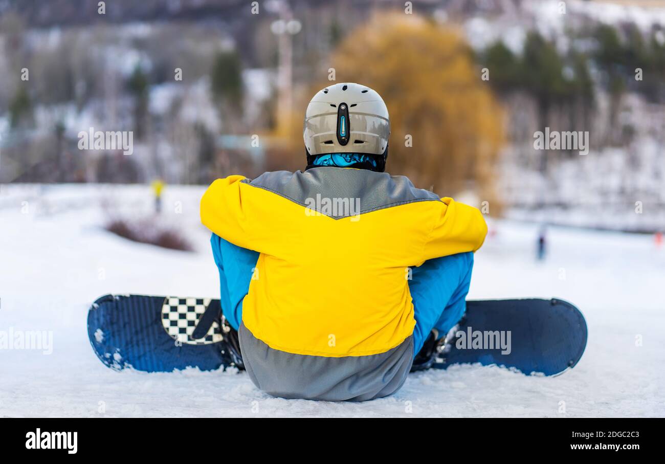 Back view of snowboarder sitting on snowy mountain Stock Photo