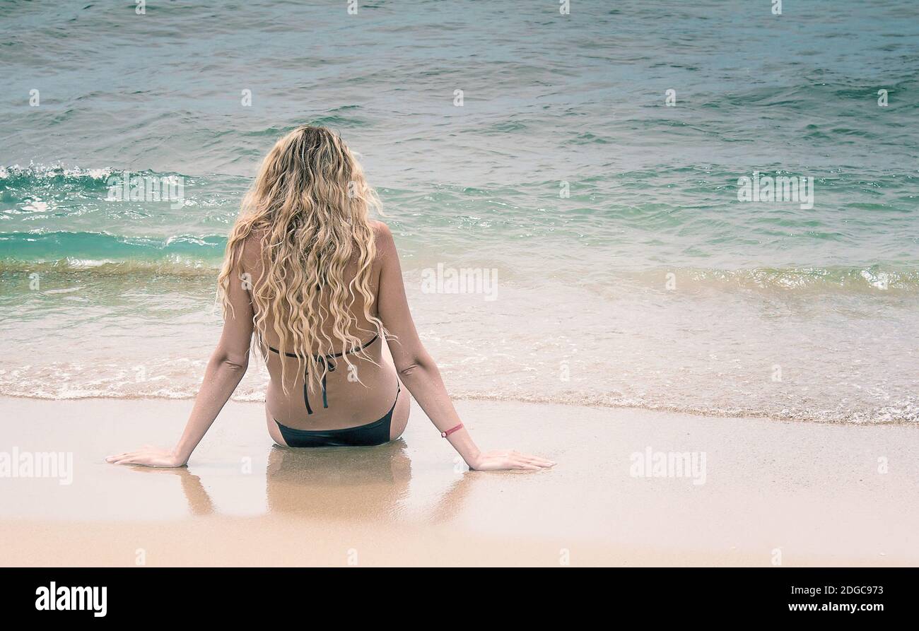 The young girl sits by the sea near water. Stock Photo