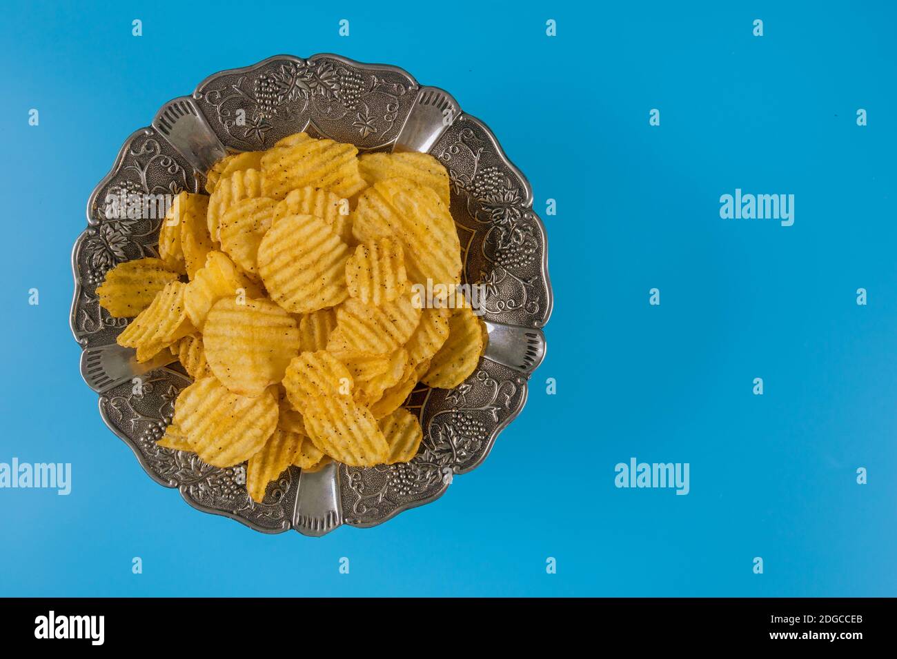 Potato chips in silver bowl on a blue background, top view. Stock Photo