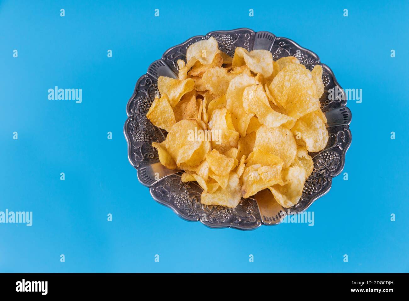 Crispy potato chips in a silver bowl on blue background. Stock Photo