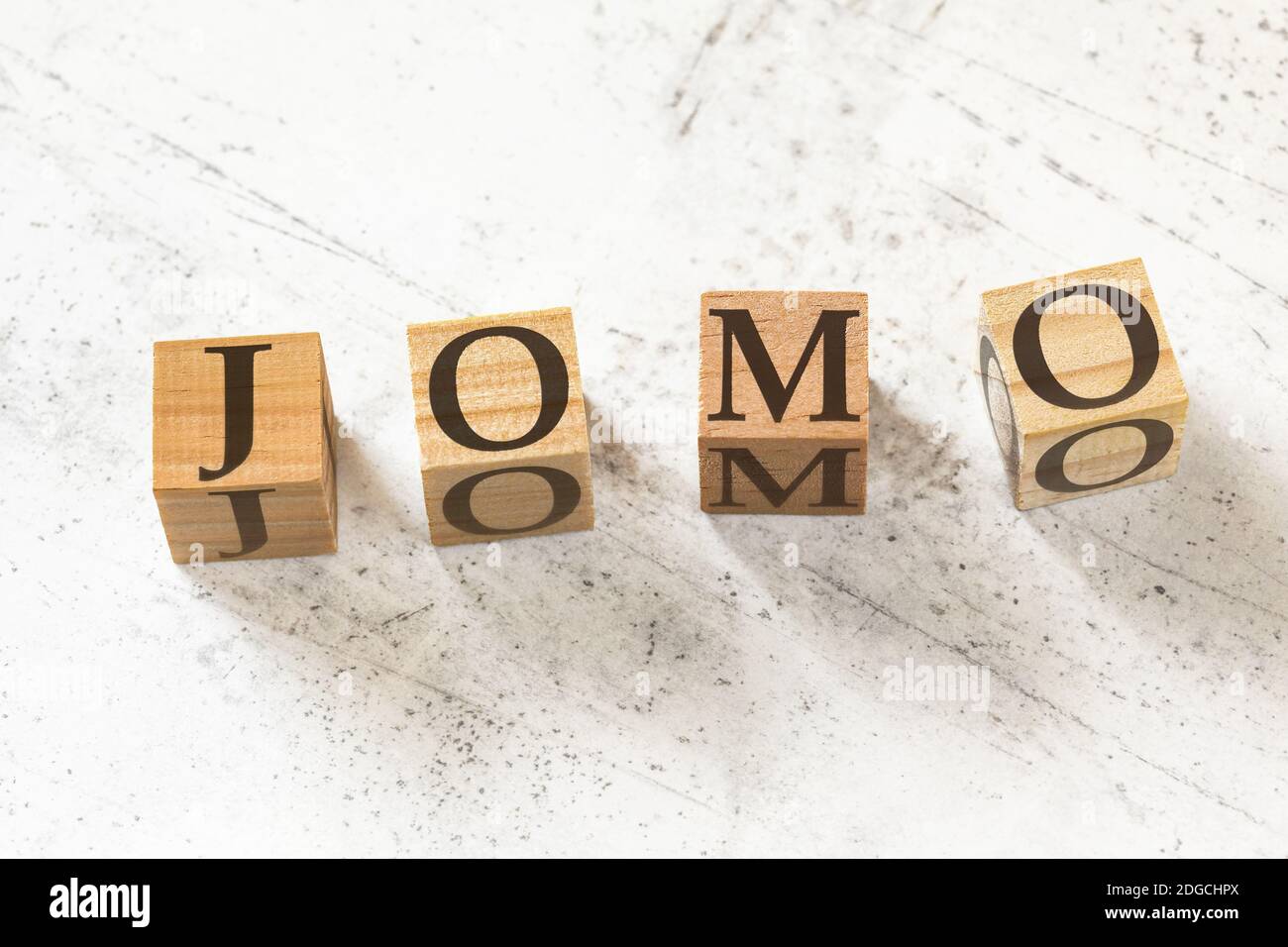 Four wooden cubes with letters JOMO (meaning Joy of missing out) on white working board. Stock Photo