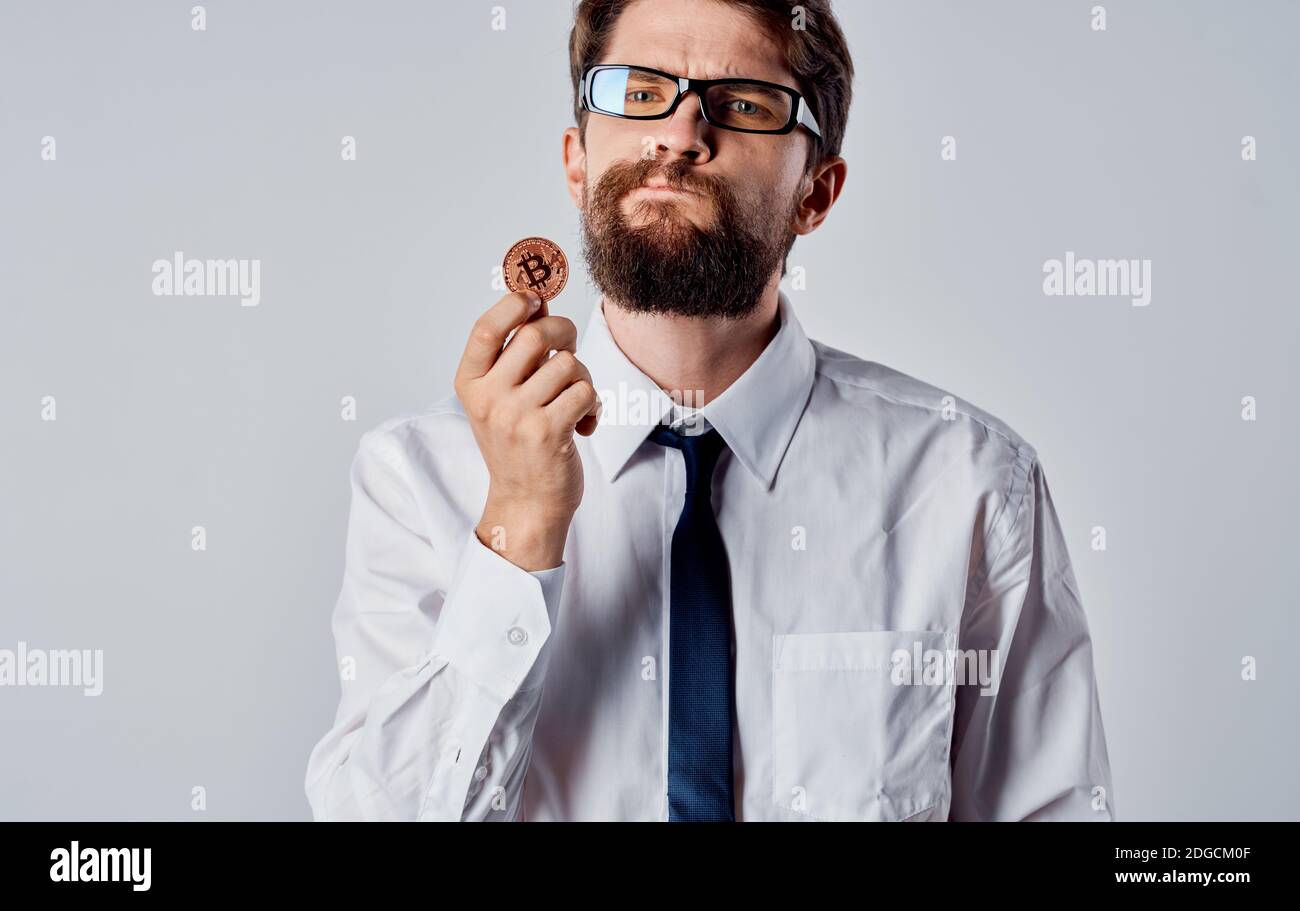 A man with a gold coin in his hands on a light background puzzled look