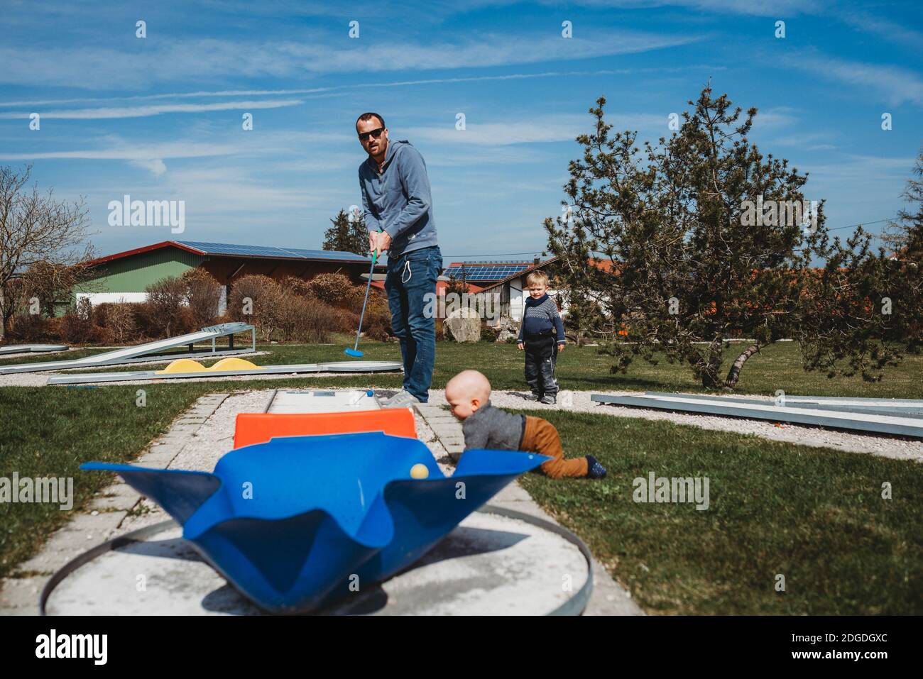 Father and son playing mini golf in farm on sunny day Stock Photo