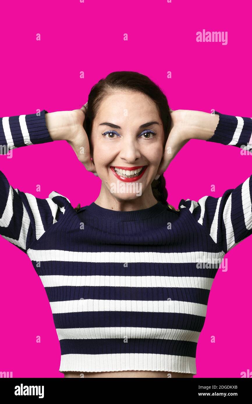 Funny woman covering her ears looking camera with toothy smile, happy, joyful over purple. Stock Photo