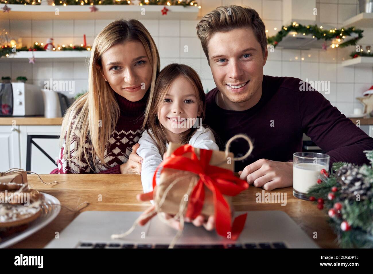 Happy parents with kid daughter giving Christmas gift to camera, web cam view. Stock Photo