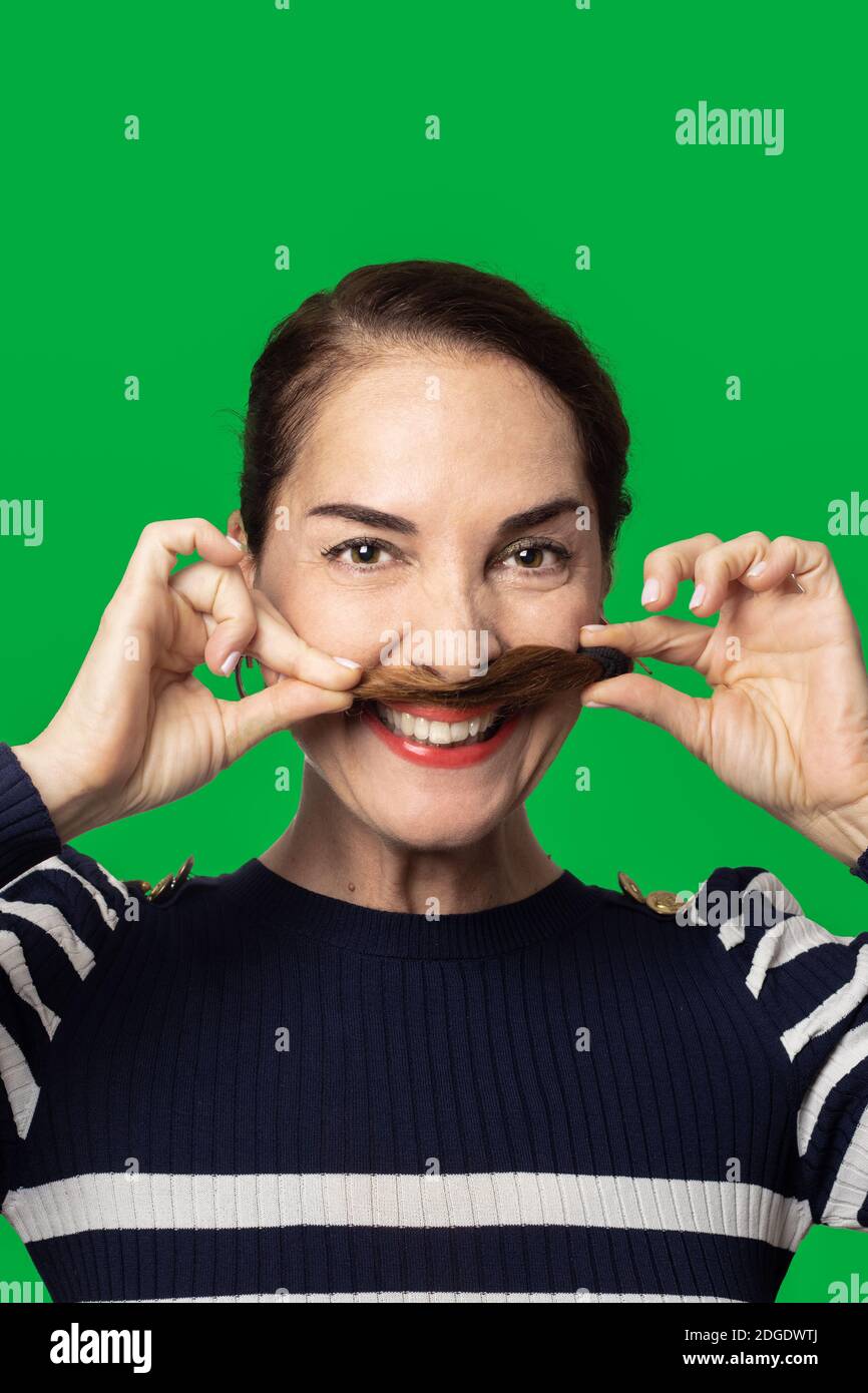 Funny woman making a mustache with her hair with toothy smile happy, over green background Stock Photo