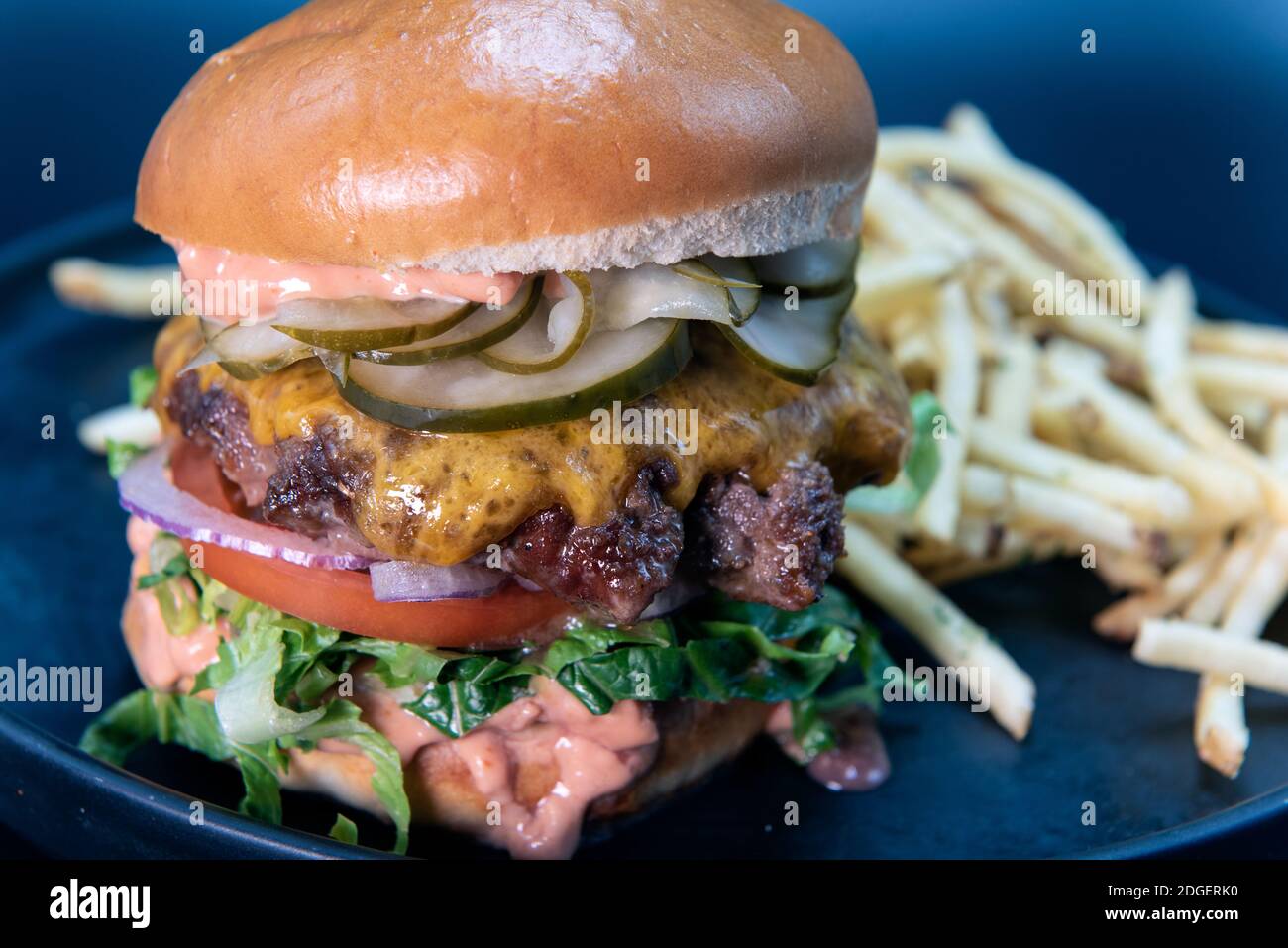 Tall order of cheeseburger and french fries loaded with all the toppings that the hamburger buns can hold Stock Photo