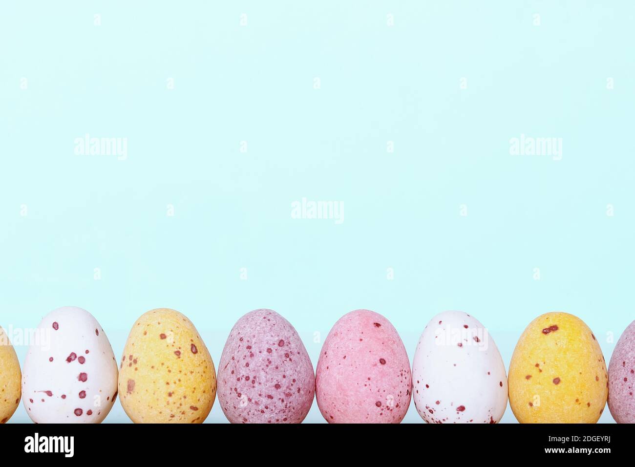 Funny kid's Easter border. Easter card with colorful eggs on light blue background. Copy space. Close-up. White yellow pink eggs for Easter treat.  Stock Photo