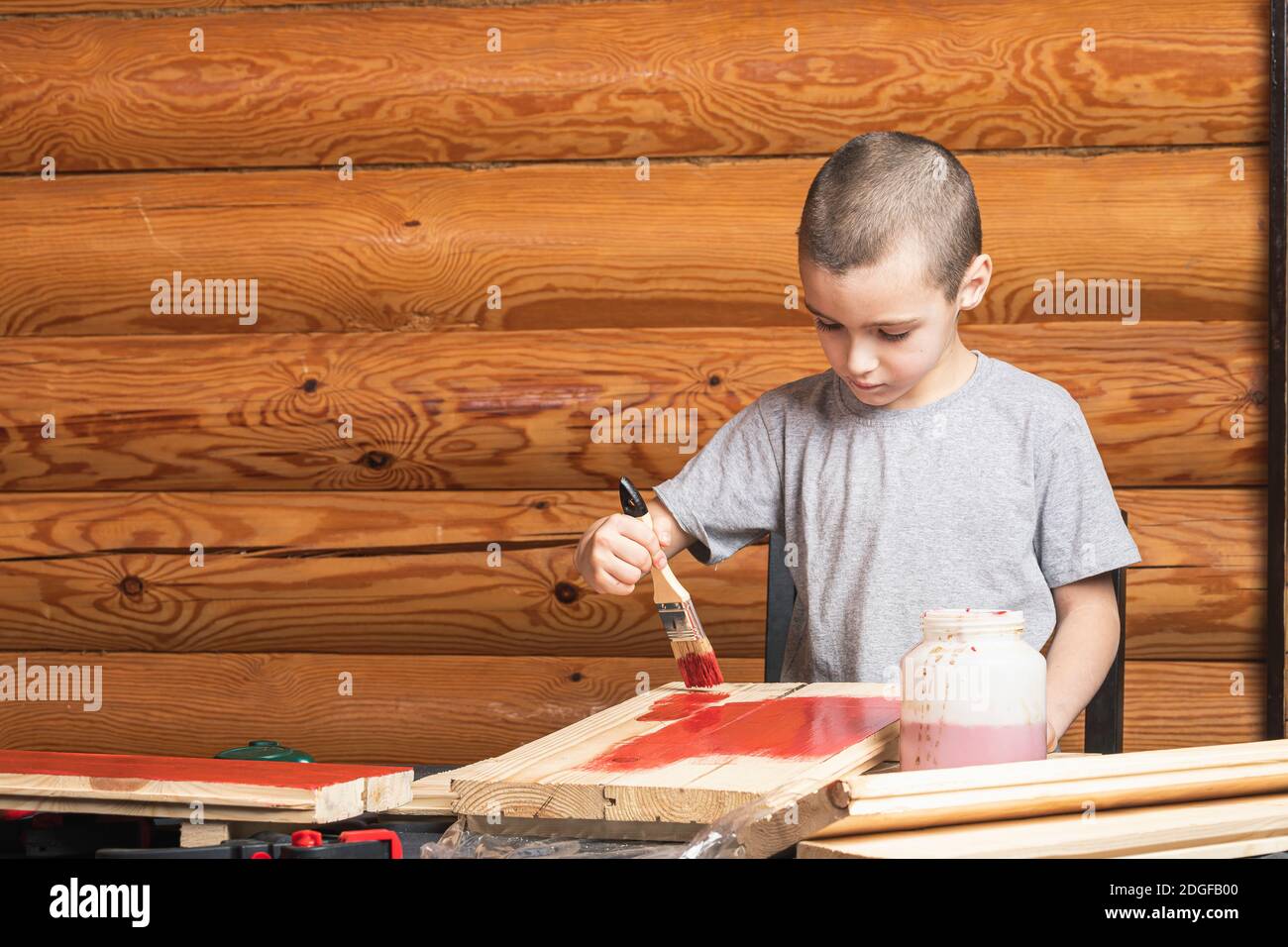 A boy paints a wooden fake with a paintbrush in red in a country house. DIY painting the walls. Teenage artist doing home renovations. Stock Photo