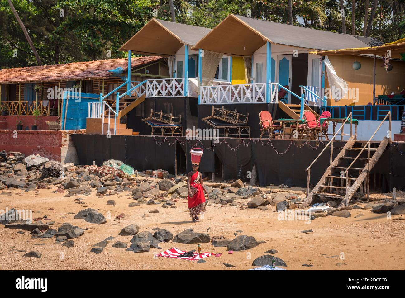 PALOLEM, GOA, INDIA - MARCH 19, 2019: Indian woman in traditional dress saree carries a bucket on her head along the village houses on the shore of th Stock Photo