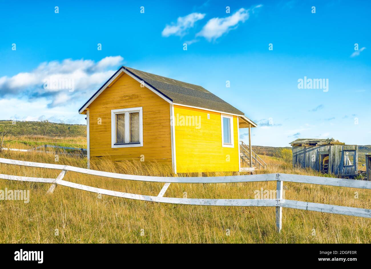 Abandoned yellow small house with white fence in countryside Stock Photo