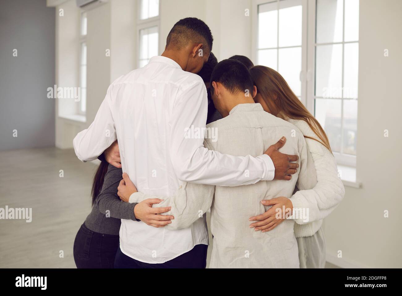 Team of young colleagues or students standing in circle and embracing each other Stock Photo