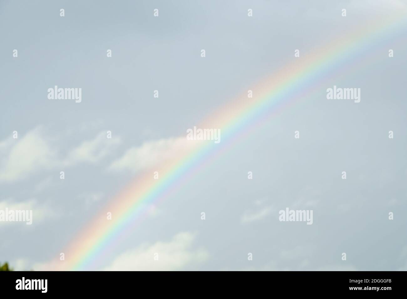 Delicate summer rainbow on the blue sky after the rain. Stock Photo
