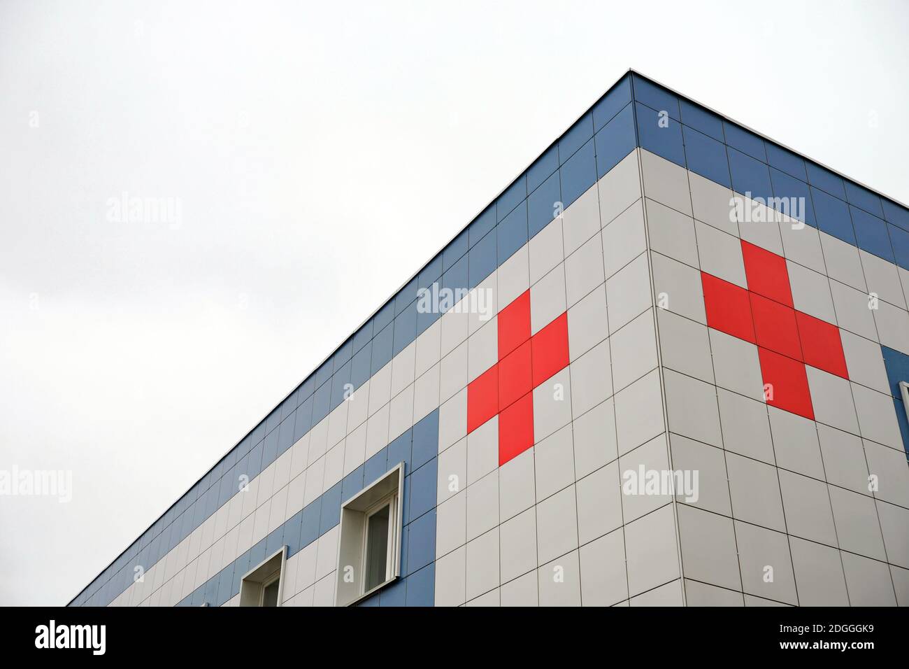 Medical symbol red cross on the cladding of the hospital building against the background of the cloudy sky. Stock Photo