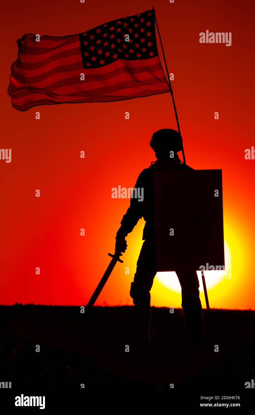 Silhouette of American army soldier armed sword and shield standing under waving US national flag on background of sunset. Army hero and patriot, military glory and honor, fallen soldiers remembrance Stock Photo
