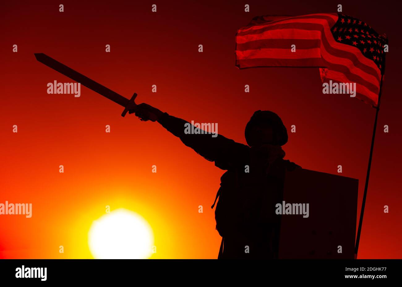 Silhouette of USA army soldier standing under national flag, holding shield, raising and pointing sword forward on sunset background. Soldier duty and honor, national hero and military victory concept Stock Photo