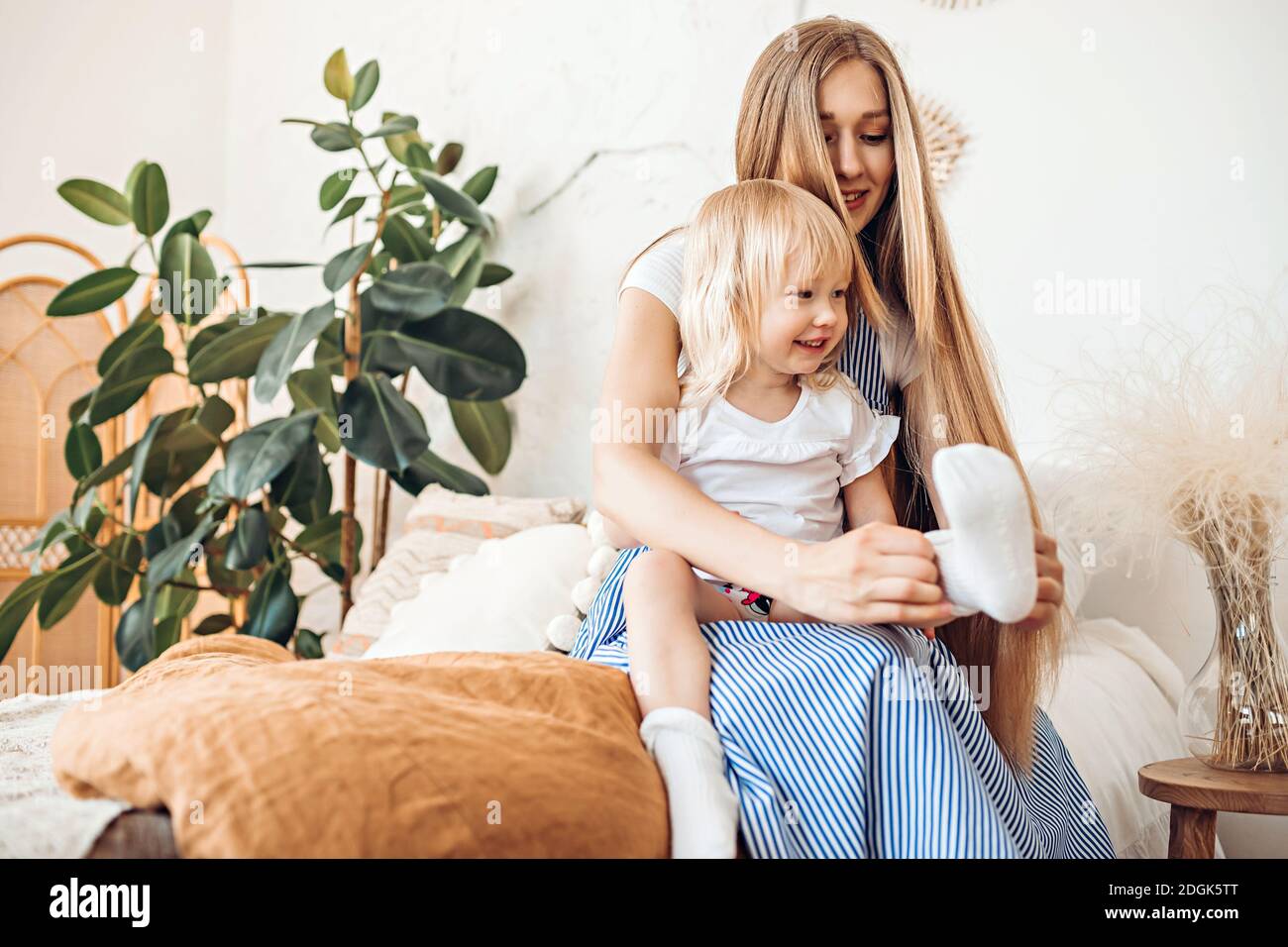 Young mom or babysitter puts on socks to a three year old child Stock Photo