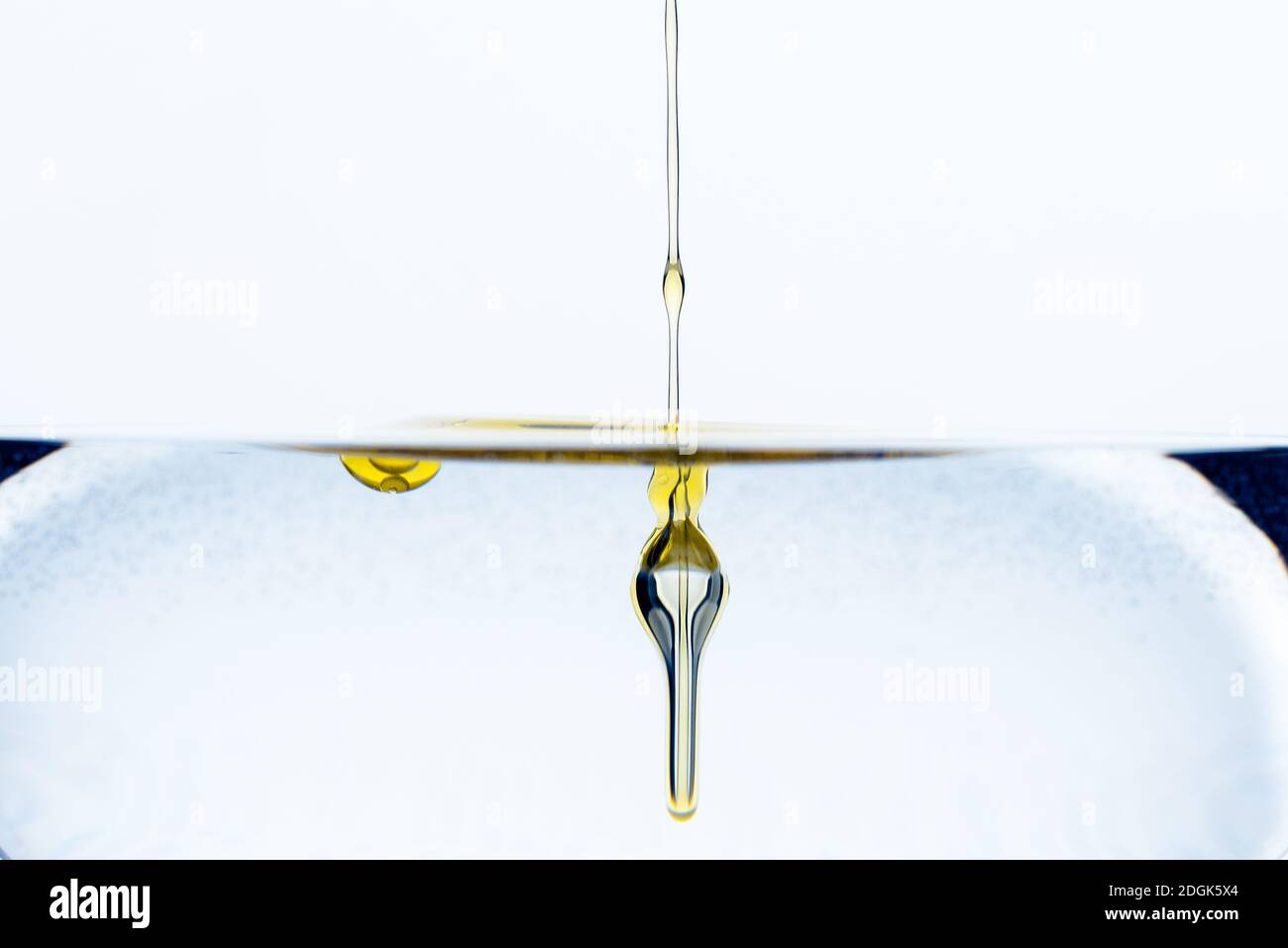 Detail of dash of olive oil drops gliding into glass of water isolated