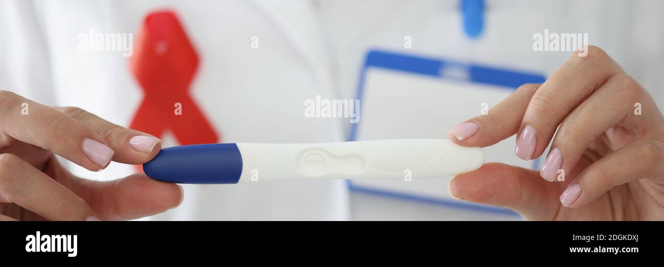 Doctor's hands with red ribbon on his chest hold pregnancy test closeup