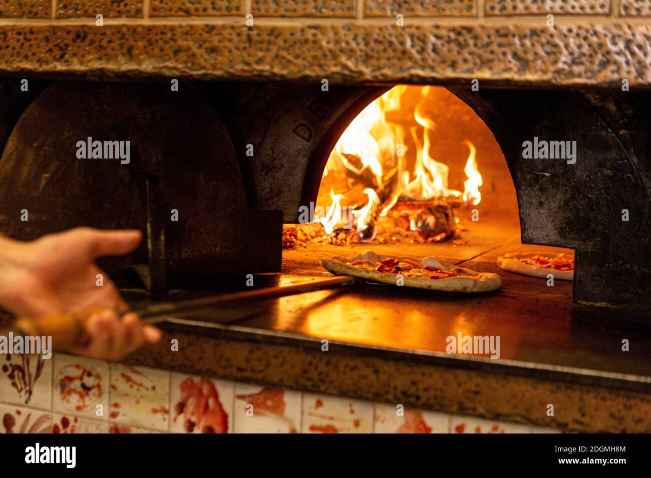 A pizza is placed into a wood burning oven in a restaurant in Rome Stock Photo