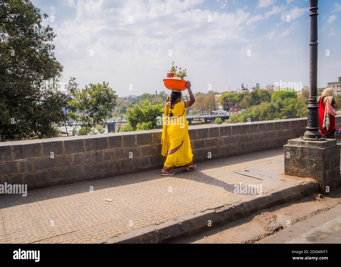 PUNE, INDIA - MARCH 14, 2019: Woman in yellow national dress saree carries on her head a basin with pots of flowers in Pune, India Stock Photo