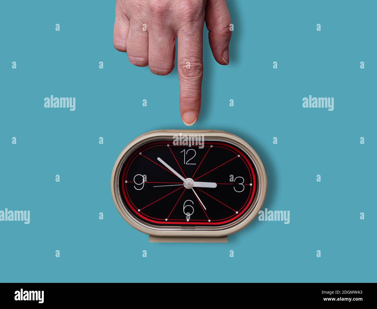 Female finger turning off analog retro alarm clock on cyan background