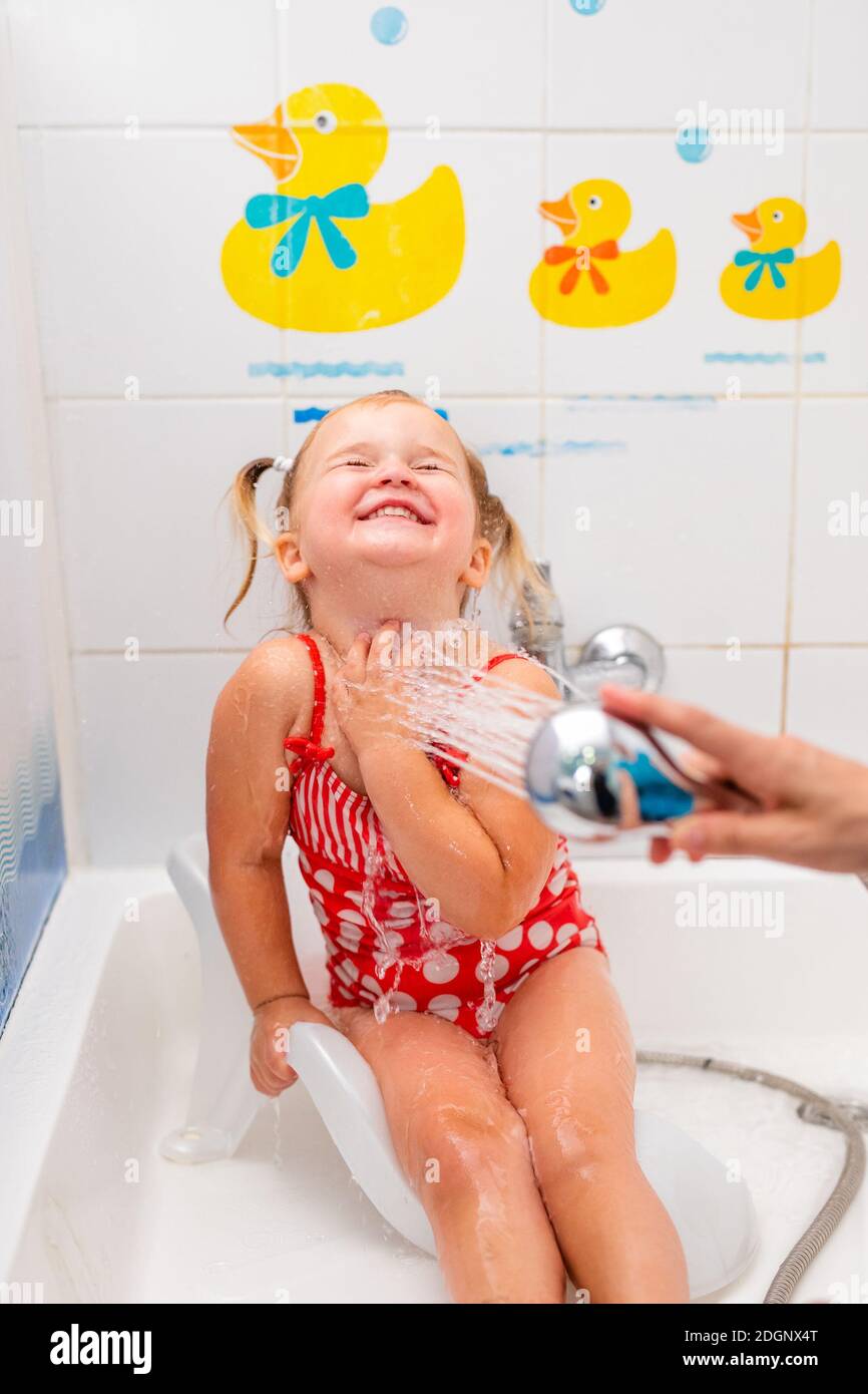 Toddler girl in a red swimsuit takes a shower before going to the pool