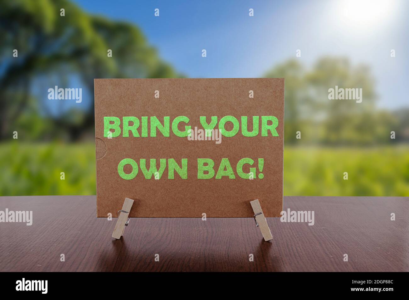 Bring your own bag text on card on the table with sunny green park background. Ecology concept, recycle, reuse, reduce waste. Stock Photo