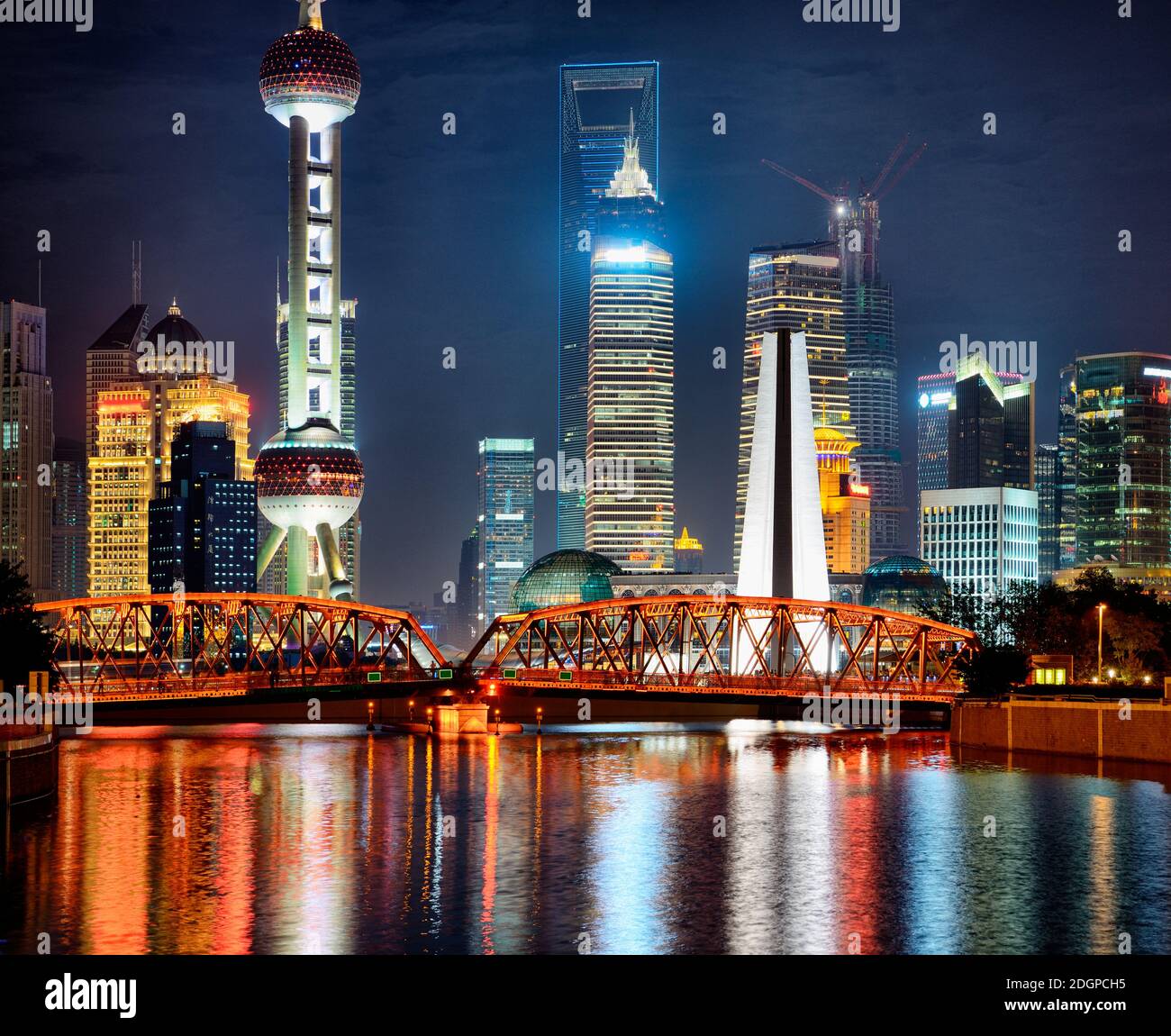 Nocturne view at Pudong with Oriental Pearl Tower, Financial and Jin Mao towers. In foreground illuminated bridge reflection in Suzhou Creek water. Stock Photo