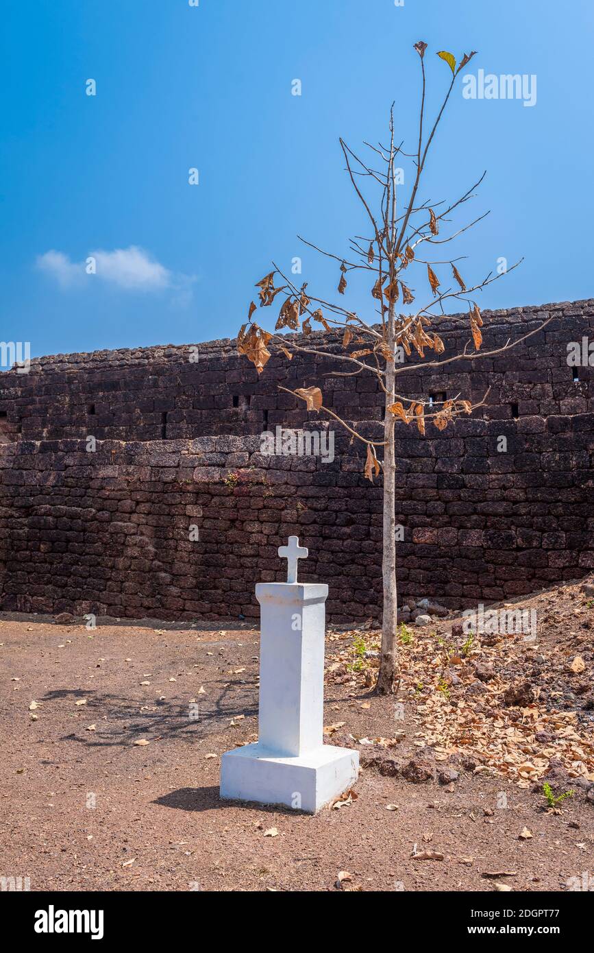 Fortress wall, tree and small white column with cross and without inscriptions in 19th century Fort Cabo de Rama built by Portuguese colonizers in Goa Stock Photo