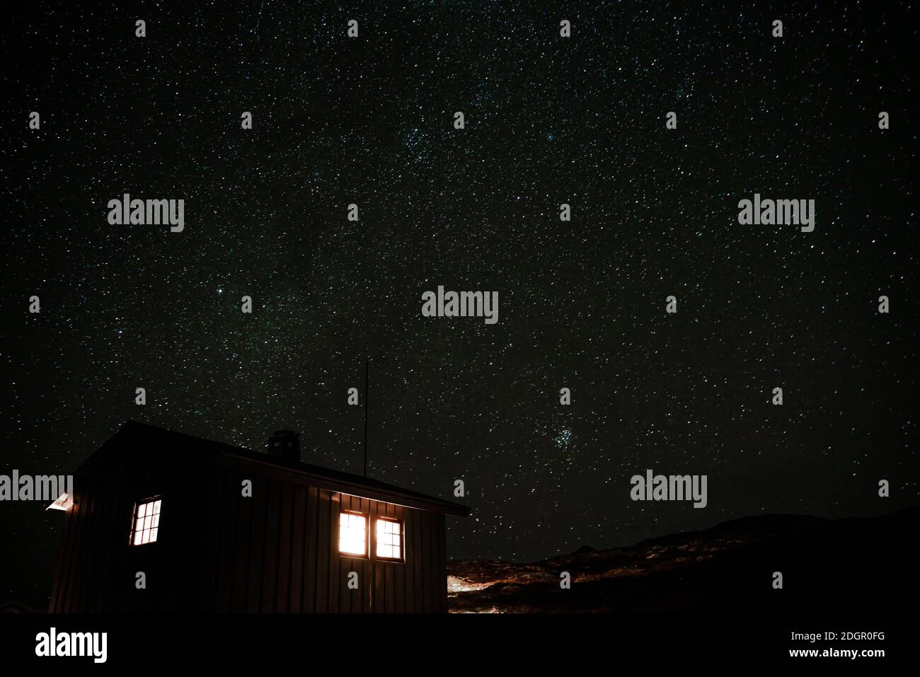 Small cabin in the mountains with light shining out the windows and a starry night sky in the background. Time lapse video.  Stock Photo