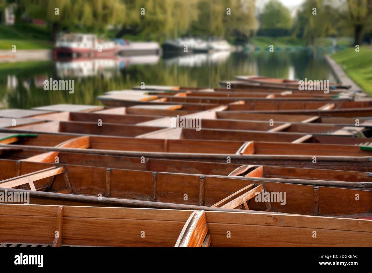 Row of empty Punts moored on the River Cam with defocused boats in the background Stock Photo