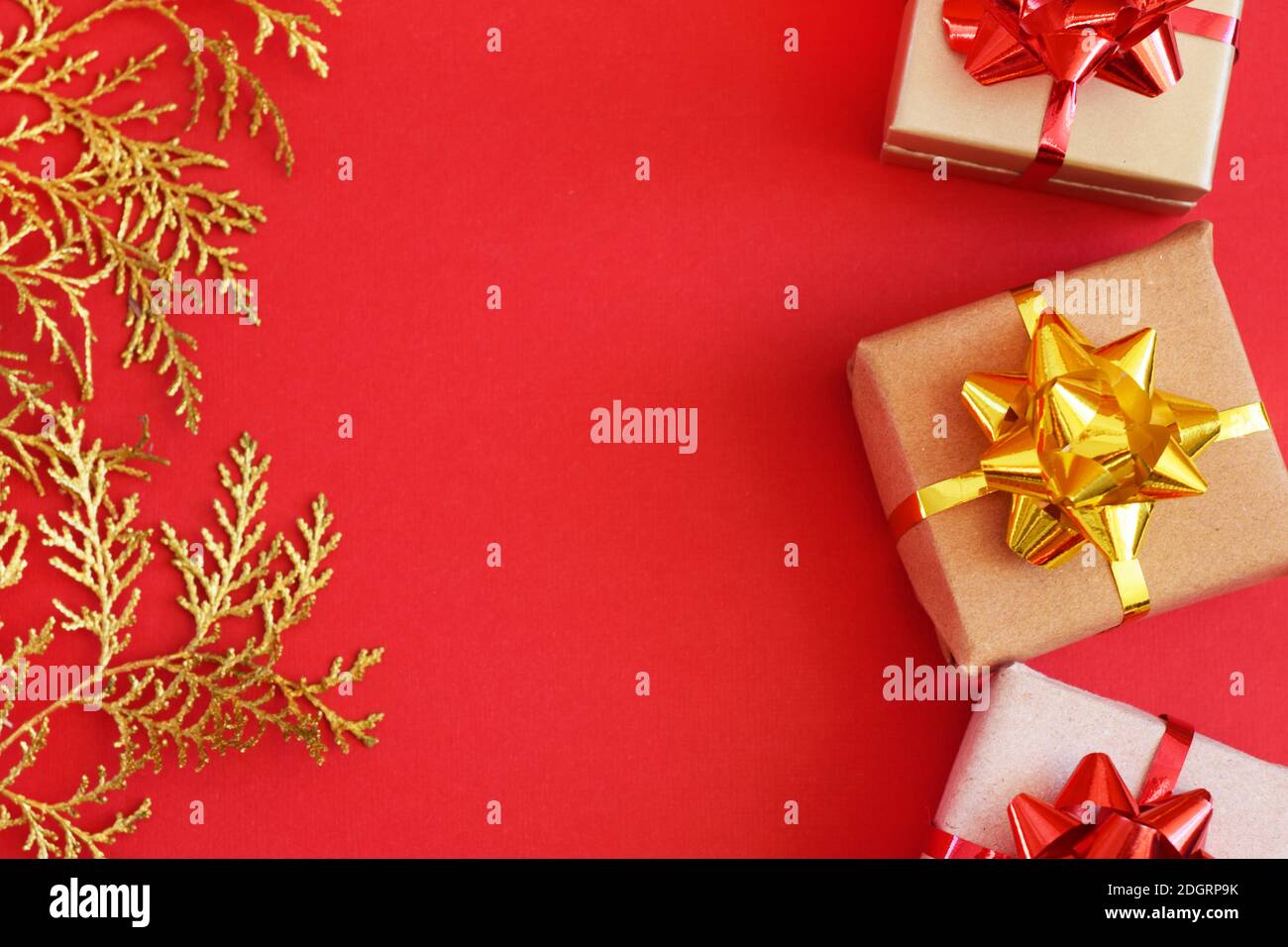 DIY handmade Christmas gift boxes in craft paper. Boxes on a red background and golden sprigs on a red background. Copy spase Stock Photo