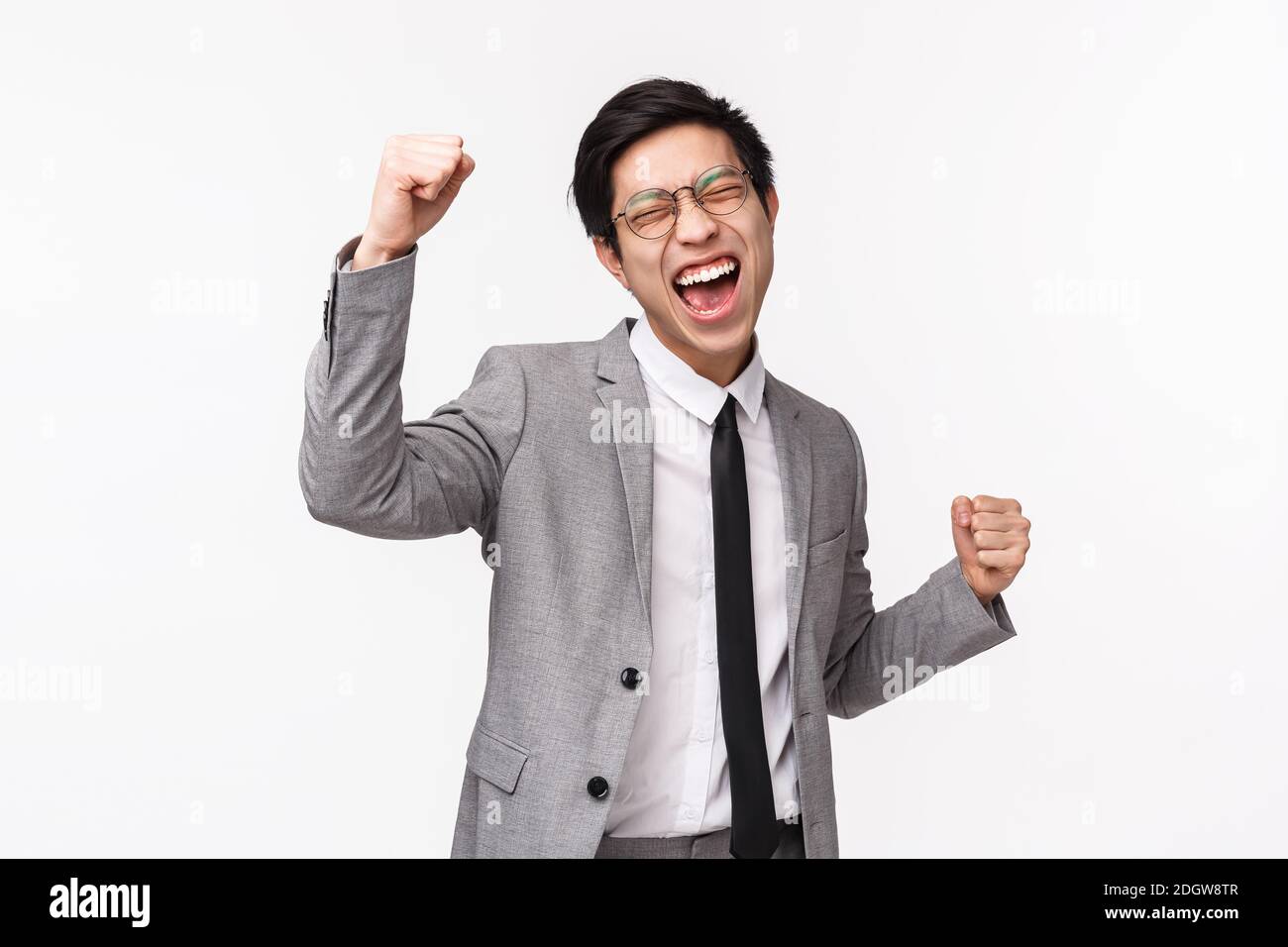 Waist-up portrait of relieved, successful asian young businessman, male entrepreneur in gray suit, fist pump, do champion dance, Stock Photo